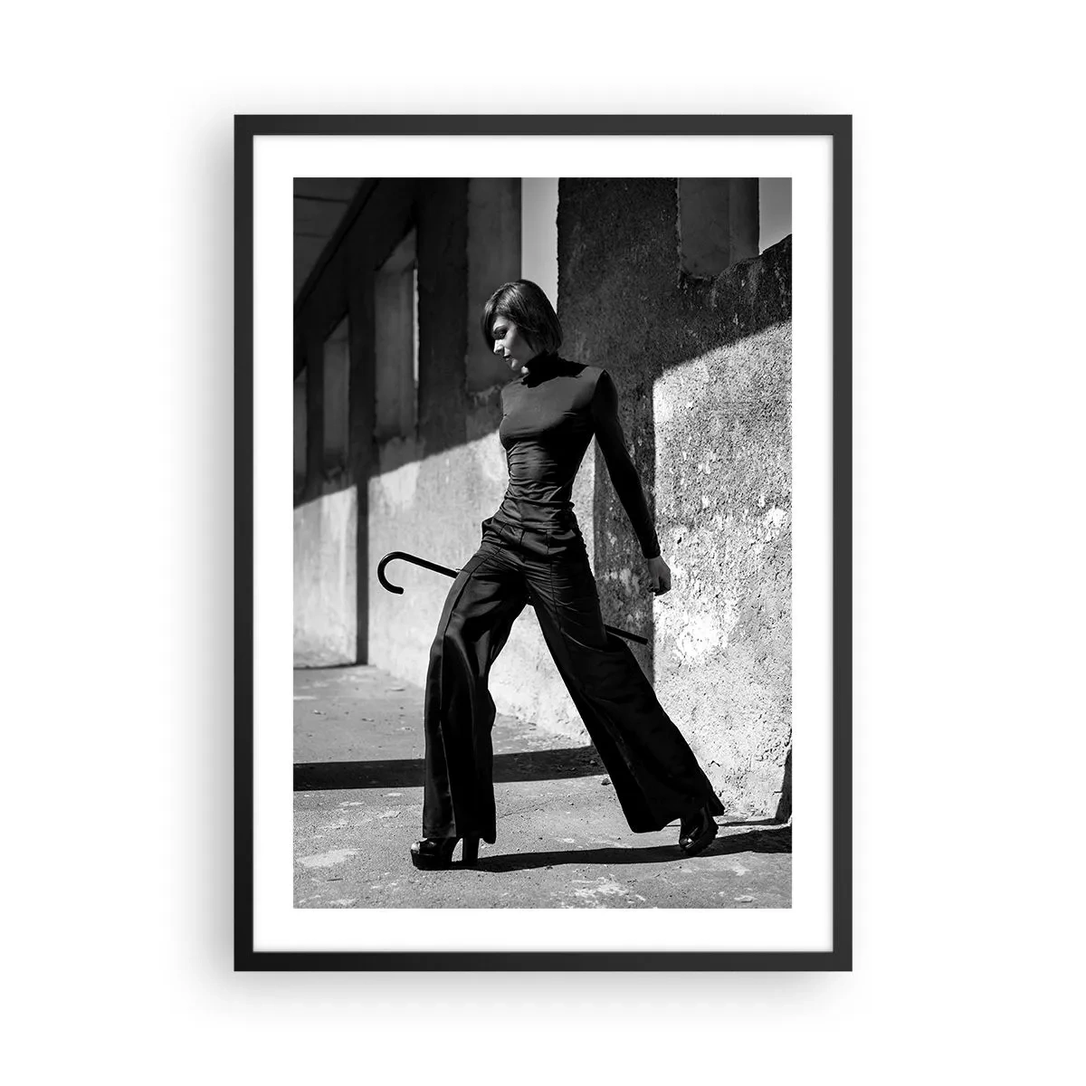 Poster în ramă neagră - O femeie într-o ținută elegantă cu un baston pe fundalul unei arhitecturi austere - 50x70cm - Eleganță urbană - Decorațiune modernă pentru perete pentru living și dormitor ARTTOR