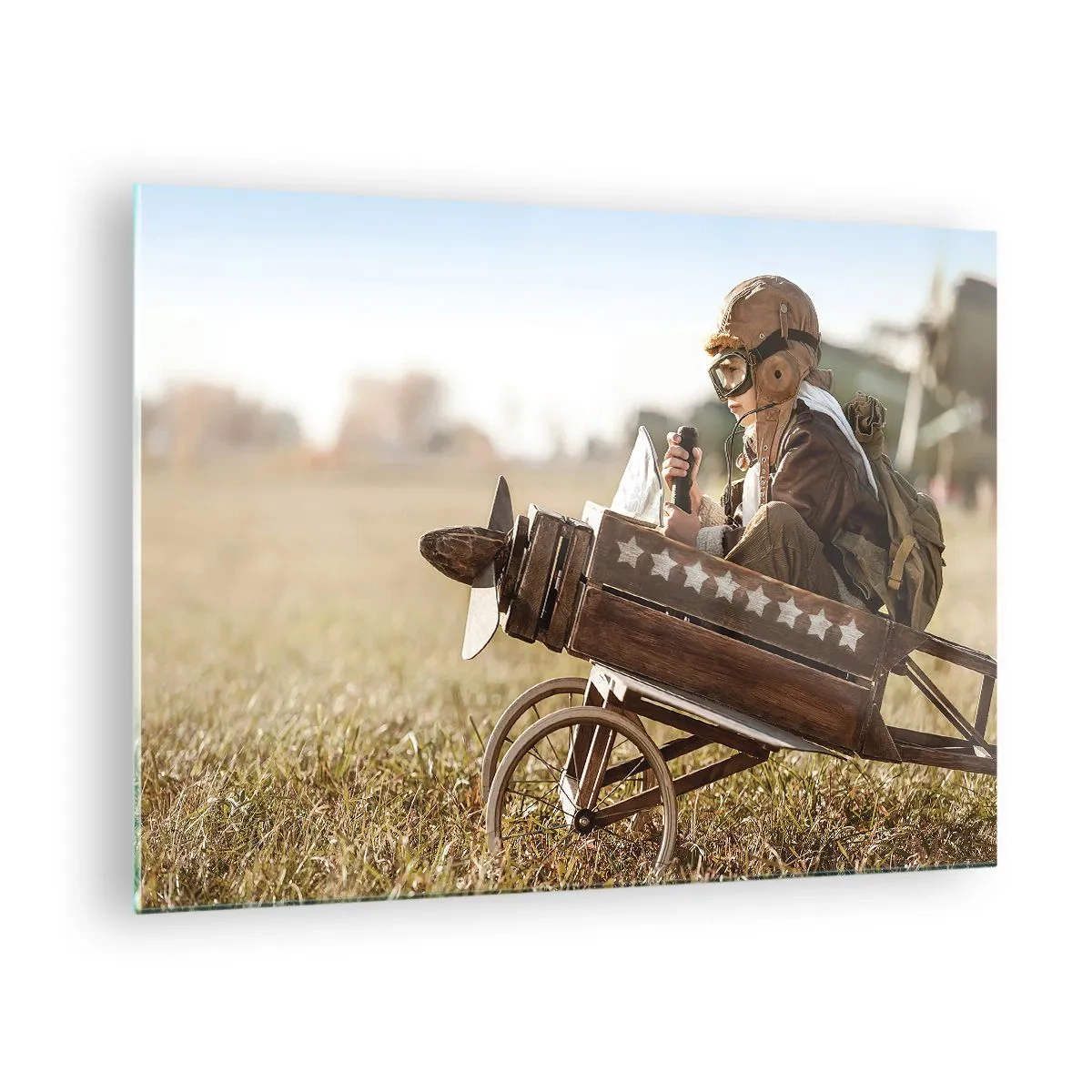 Tablou pe sticlă - Un copil într-un avion de lemn, prefăcându-se a fi pilot, purtând haine de aviator. - 70x50cm - Porniți spre vis - Decorațiune modernă pentru perete pentru living și dormitor ARTTOR